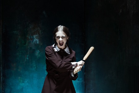 Portrait of a young girl with baseball-bat in school uniform as killer woman against school board ....