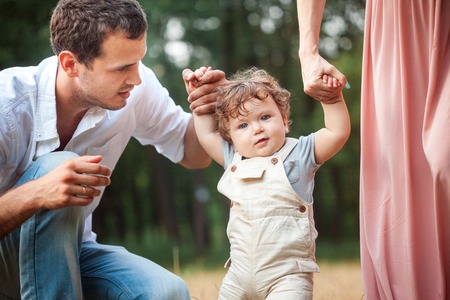 Young beautiful father, mother and little toddler son against green trees. Happy family with her...