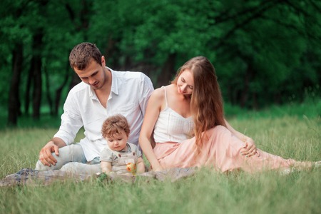 Young beautiful father, mother and little toddler son against green trees. Happy family with her...