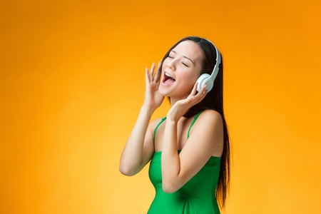 The cute cheerful girl listening to music on headphones on orange backgroundの写真素材