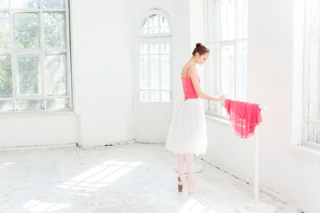 Ballerina in white and red dress posing in pointe shoes at white wooden pavilionの写真素材
