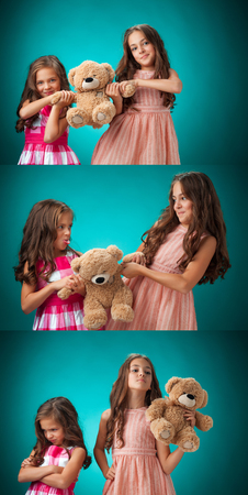 The two cute little girls with Teddy bear on blue backgroundの写真素材