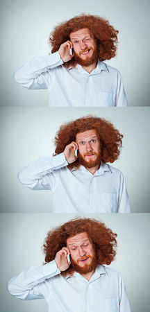 Portrait of puzzled man with long red hair, talking on the phone on a gray background. Collageの写真素材