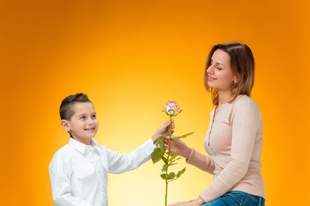 Young kid giving red rose to his mom on orange backgroundの写真素材