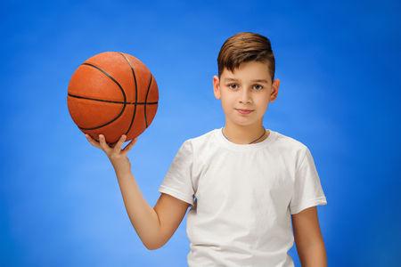 Adorable 11 year old boy child with basketball ball on blue background.の写真素材