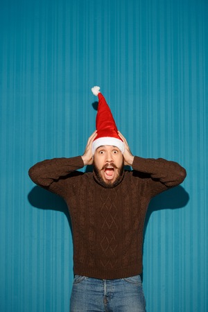 The surprised christmas man wearing a santa hat on the blue studio backgroundの写真素材