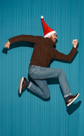 The running christmas man wearing a santa hat on the blue studio backgroundの写真素材