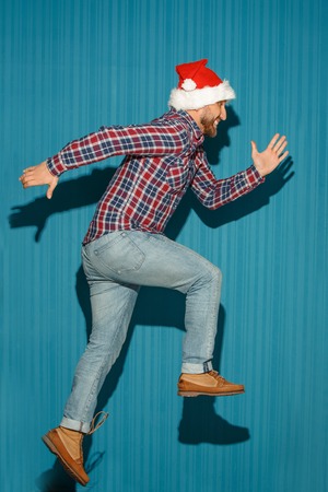 The running christmas man wearing a santa hat on the blue studio backgroundの写真素材