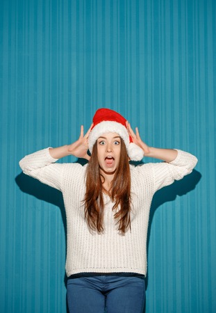 The surprised christmas girl wearing a santa hat on the blue studio backgroundの写真素材