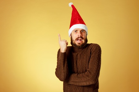 The surprised christmas man wearing a santa hat on the orange studio background pointing upの写真素材