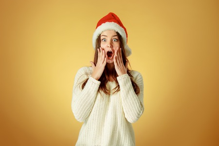 The surprised christmas girl wearing a santa hat on the orange studio backgroundの写真素材
