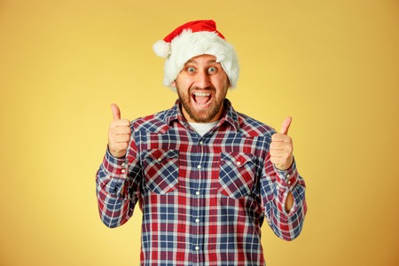 Smiling christmas man wearing a santa hat on the orange studio background with sign OKの写真素材