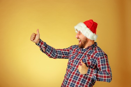 Smiling christmas man wearing a santa hat on the orange studio background with sign OKの写真素材