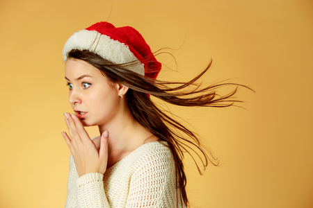 The surprised christmas girl wearing a santa hat on the orange studio backgroundの写真素材