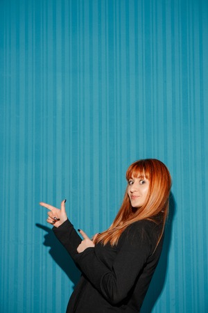 Portrait of young woman with shocked facial expression over blue studio background pointing on the leftの写真素材