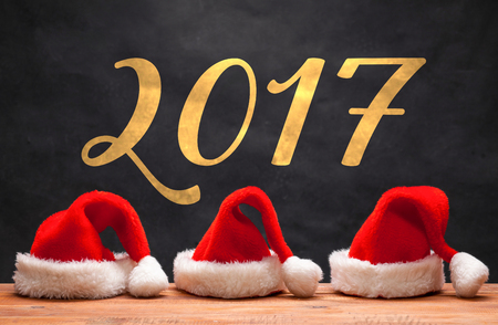 The three Santa red hats on wooden table on black background