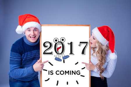 Christmas couple holding white board with empty copy space over blue background. Concept of...