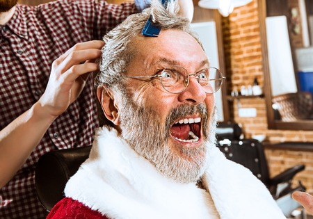 The senior man in Santa claus costume shaving his personal master at barber shop before Christmasの写真素材