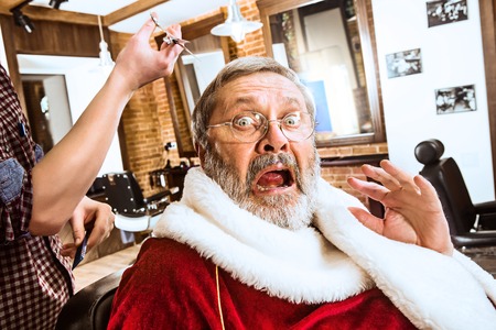 The senior man in Santa claus costume shaving his personal master at barber shop before Christmasの写真素材