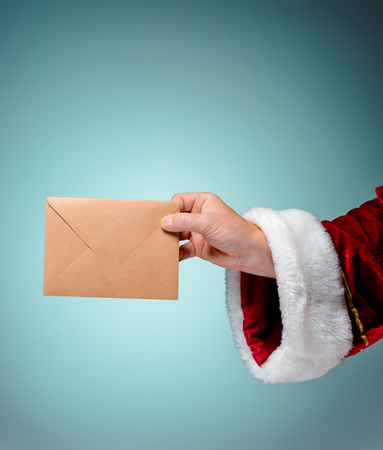 Hand in costume Santa Claus is holding the envelope on blue studio background. Merry Christmas and New Year's conceptの写真素材
