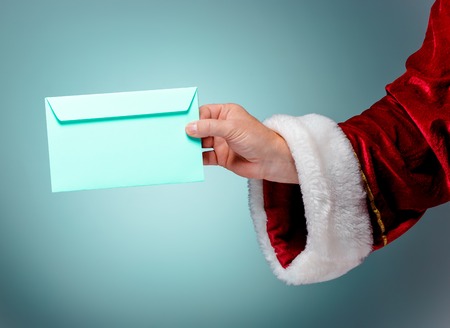 Hand in costume Santa Claus is holding the envelope on blue studio background. Merry Christmas and New Year's conceptの写真素材