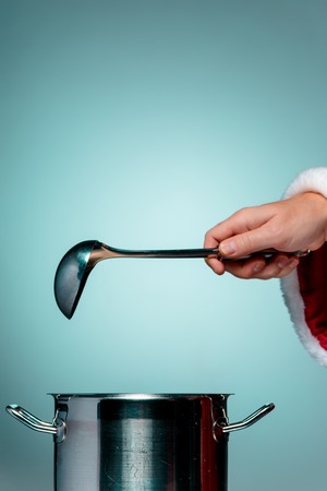The Santa hand holding a ladle or kitchen spoon and ready for Christmas time on blue studio backgroundの写真素材
