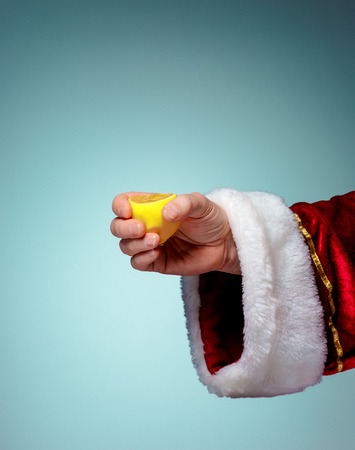 Photo of Santa Claus Hand squeezing lemon on blueの写真素材