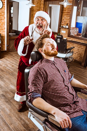 The senior man in Santa claus costume working as personal master with scissors at barber shop before Christmasの写真素材