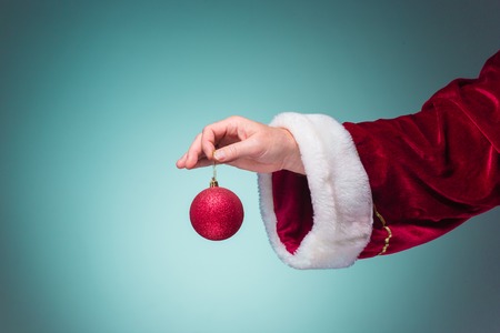 The hand of santa claus holding a Christmas ball on blue background