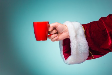 The hand of santa claus holding a red cup on blue backgroundの写真素材