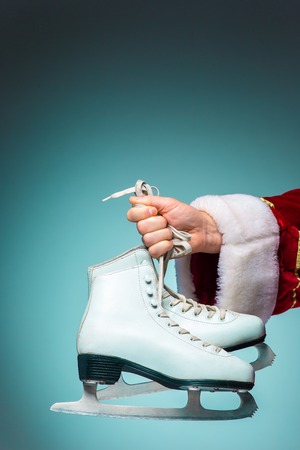 The hand of santa claus holding a figure skates on blue backgroundの写真素材