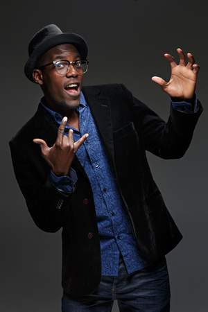 The portrait of handsome young black african smiling man in hat on dark background. Positive human emotionsの写真素材