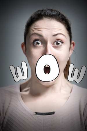 Portrait of young woman with shocked  and surprised facial expressions  over gray backgroundの写真素材