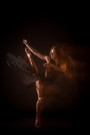 Young beautiful dancer in beige dress dancing on black studio backgroundの写真素材