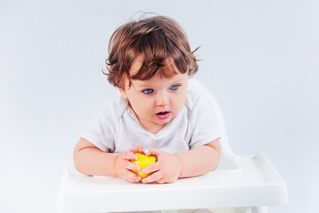 Happy baby boy sitting and eating apples fruits on gray studio backgroundの写真素材