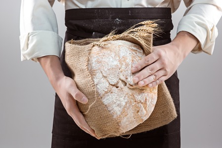 Baker man holding rustic organic loaf of bread in handsの写真素材