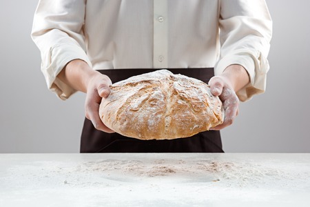 Baker man holding rustic organic loaf of bread in handsの写真素材