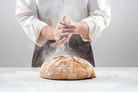 The male hands in flour and rustic organic loaf of breadの写真素材
