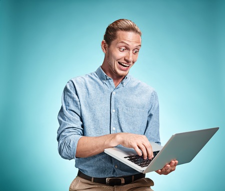 The smiling young man in a blue shirt working on laptop on blue studio backgroundinの写真素材