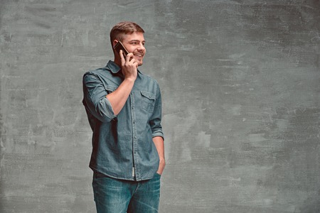 The young smiling caucasian businessman on gray background talking with phone