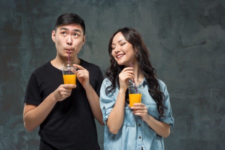 A young pretty Asian couple with a glasses of Orange juiceの写真素材