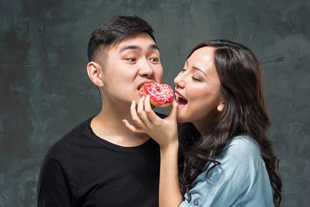 Young asian couple enjoy eating of sweet colorful donutの写真素材