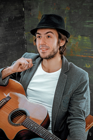 Cool guy sitting with guitar on gray backgroundの写真素材