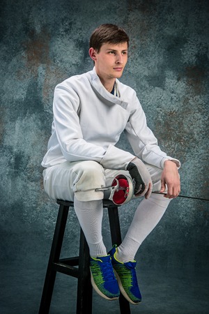 The man wearing fencing suit with sword against gray