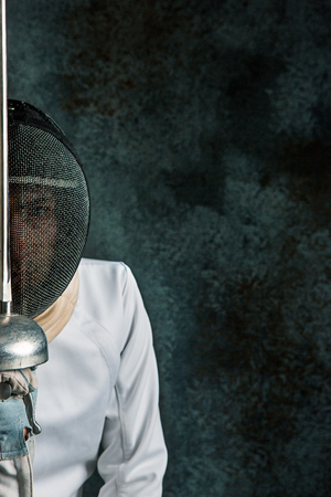 The man wearing fencing suit with sword against grayの写真素材