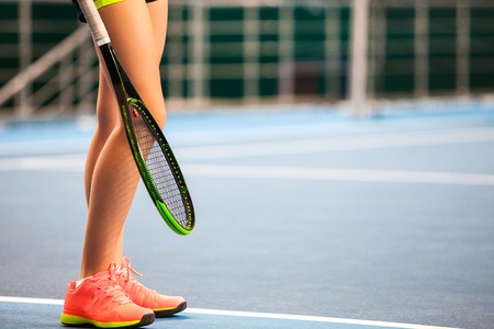 Legs of young girl in a closed tennis court with racketの写真素材