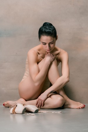 Tired ballet dancer sitting on the wooden floor on a pink backgroundの写真素材