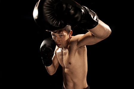 Male boxer boxing in punching bag with dramatic edgy lighting in a dark studioの写真素材