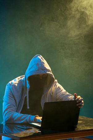 Hooded computer hacker stealing information with laptopの写真素材