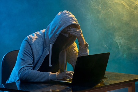Hooded computer hacker stealing information with laptop